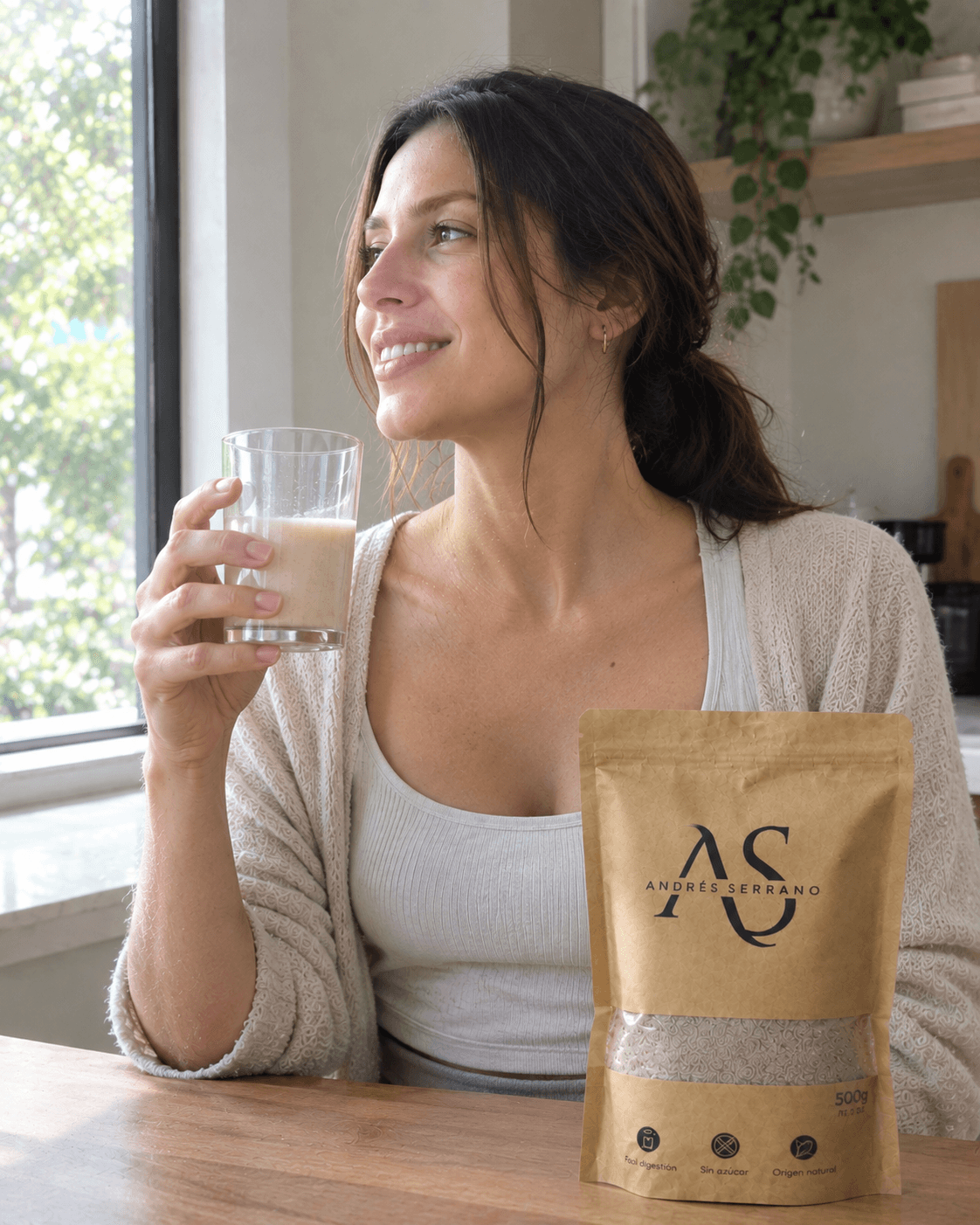 Mujer sonriendo junto a la ventana con un vaso de fibra y la bolsa sobre la mesa